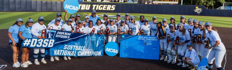 Softball players posing on softball field holding trophies.