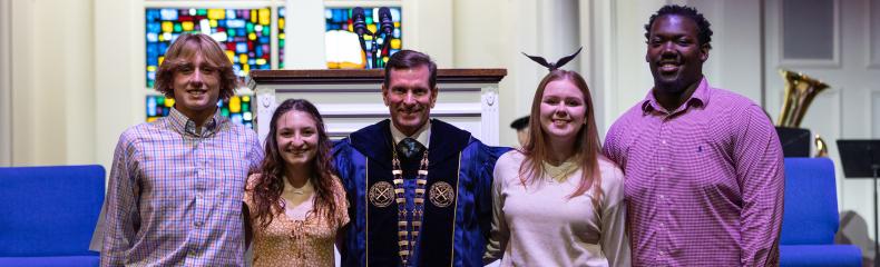 Four ETBU students pose for a photo with University President J. Blair Blackburn, who is dressed in academic regalia