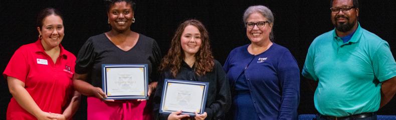 Two Students pose with awards alongside three judges on a stage