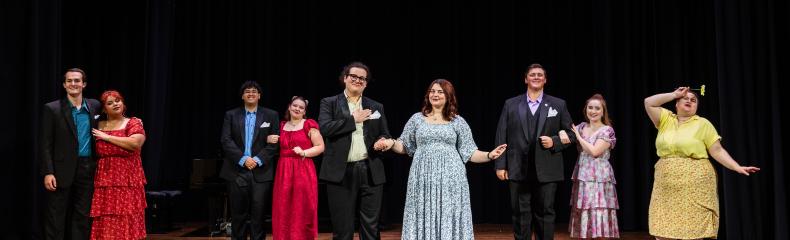 Actors stand in a line across a stage, some in pairs