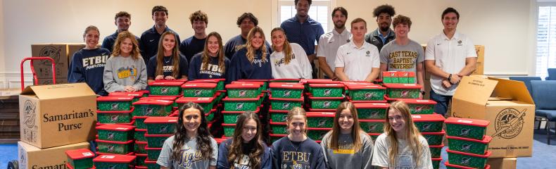 More than a dozen students stand around large stacks of Christmas boxes filled with donations