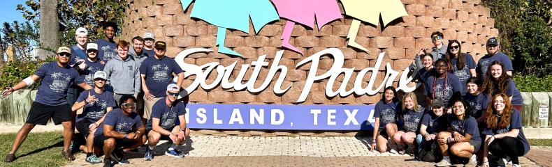 A group of people standing in front of a brick wall with South Padre Island Texas written on it