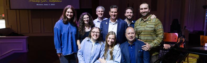 A group of people in a dark lit stage posing together, some standing, some sitting down