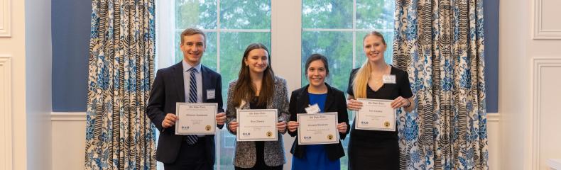 4 people stood in front of a bright window holding up awards in business professional clothing