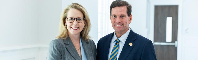 Two people stood in a brightly lit room wearing formal clothing smiling