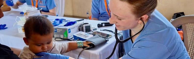 A woman tending to a pediatric patient wearing scrubs inside with a stethoscope