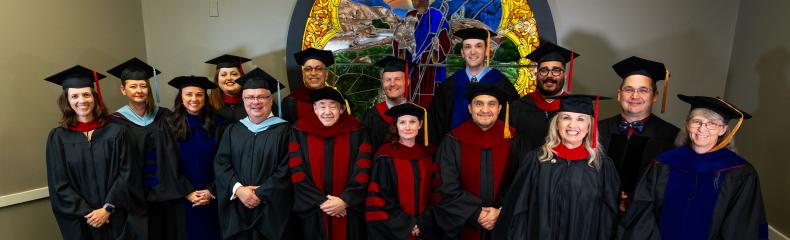 People standing inside in academic regalia infront of a stained glass window