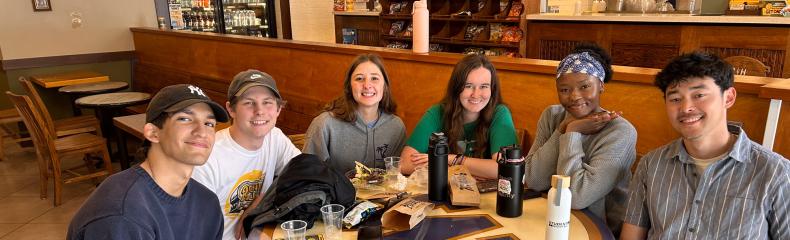 A group of people seated at a table smiling with beverages upon it