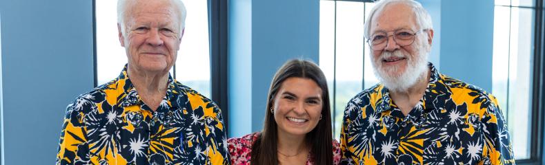 2 men and 1 woman stood smiling together in a group in floral clothing