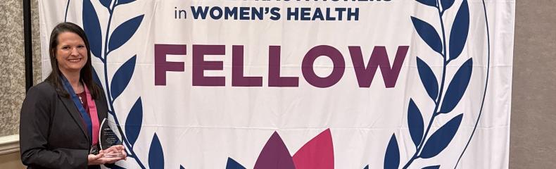 A woman in front of a backdrop sign that says the national association of nurse practitioners in womens health