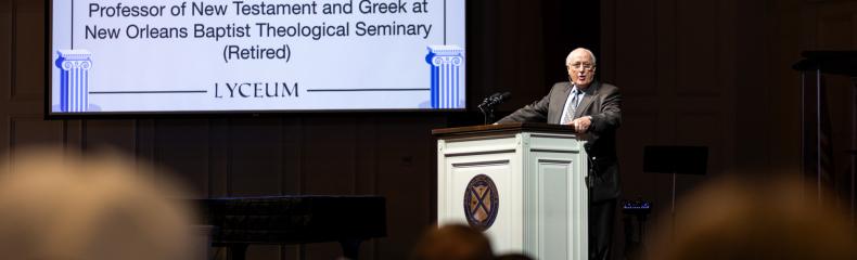 A man stood in formal attire behind a podium speaking to a crowd