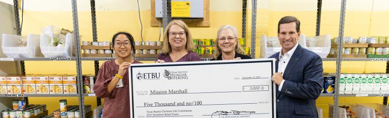 4 people holding a giant check inside a warehouse
