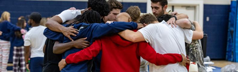 A group of men standing in a huddled circle praying