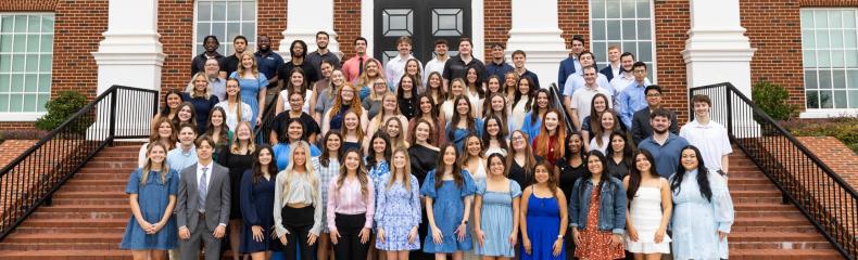 A group of people standing on the steps of a large brick building with white collumns