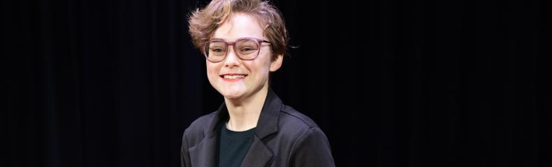 Students stands in a spotlight on a stage with a dark background