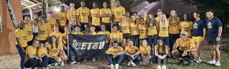 a group of people outside in yellow shirts holding an ETBU flag
