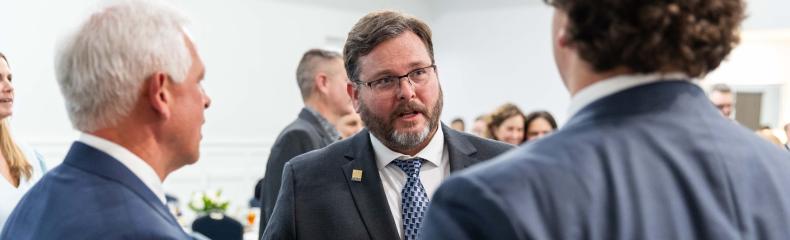 Men standing talking together in a crowded room wearing professional attire