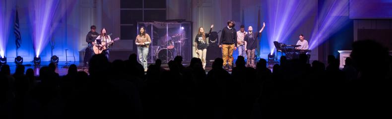 A group of people singing on a stage with a large crowd