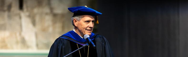 A man speaking behind a podium in academic regalia