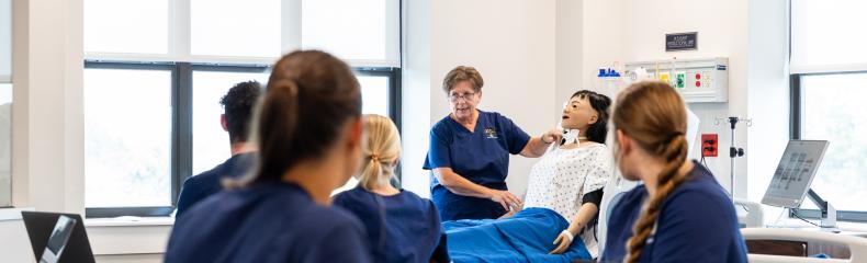 Nursing instructor with dummy teaches with students in the foreground.