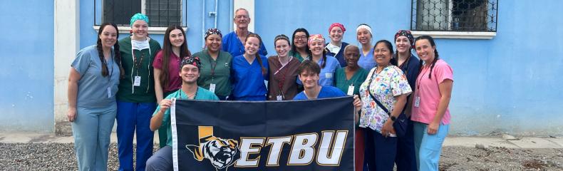 Group of people with an ETBU flag in front of a blue building.